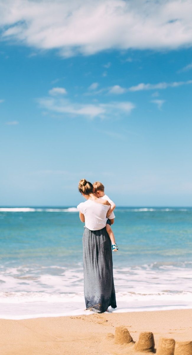 woman carrying toddler on seashore
