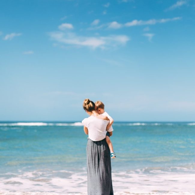 woman carrying toddler on seashore